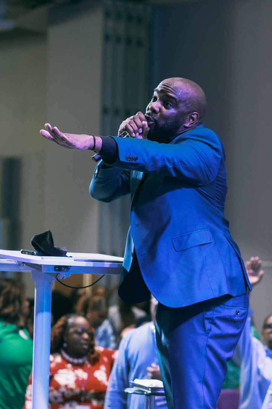 A preacher in a blue suit leaning into the crowd with a microphone